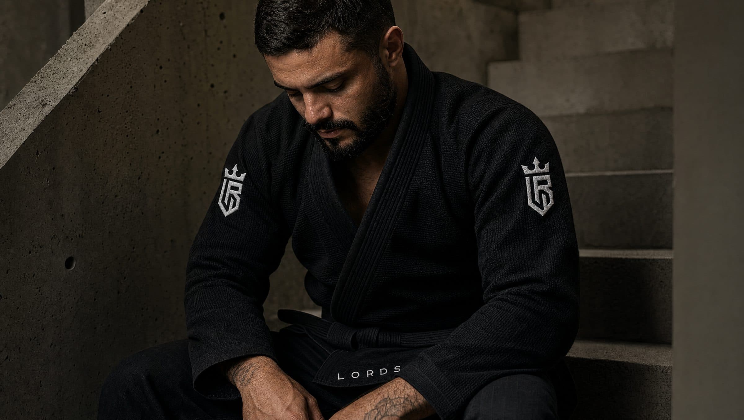Atleta sentado em degraus de concreto, vestindo kimono preto LORDS, olhar concentrado